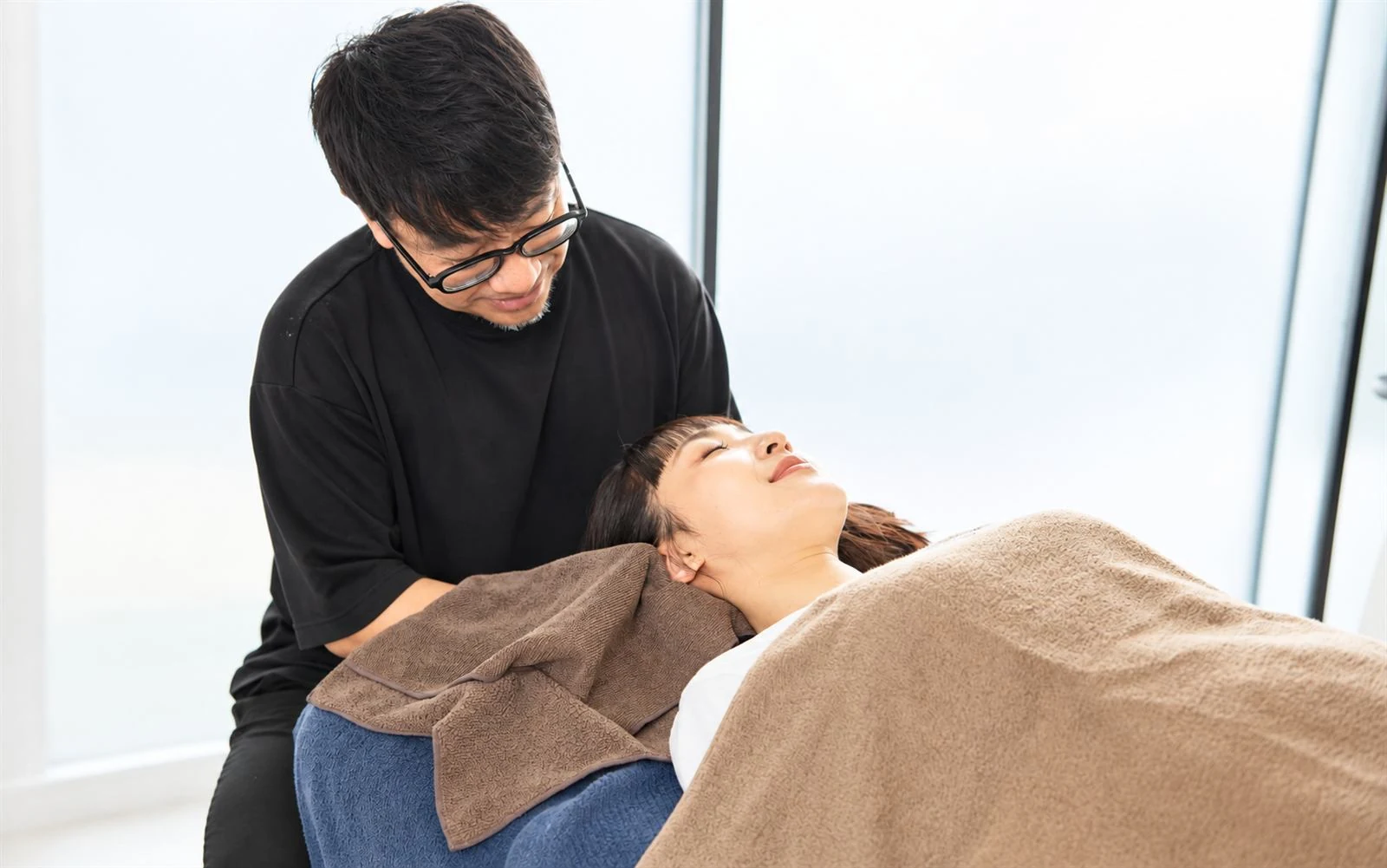 ベッドで横になるお客様の首元をトレーナーがケアしている様子