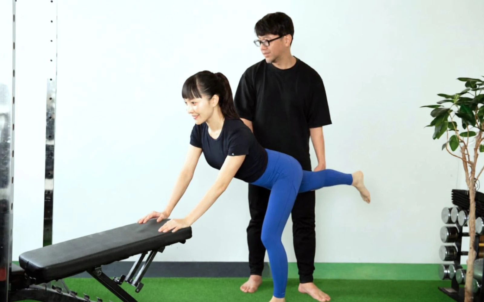 ベンチに手をつき片脚を後ろに伸ばすお客様をトレーナーが見守る様子